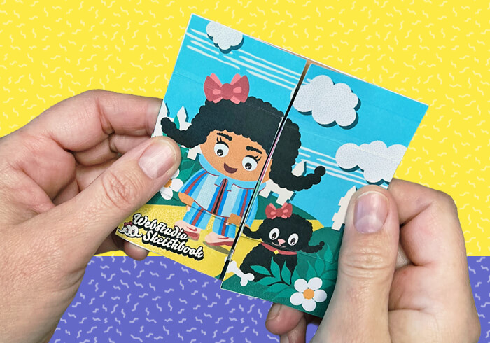 Hands holding a four-sided never-ending card with City Girls illustrations, showing the interactive paper craft in use.
